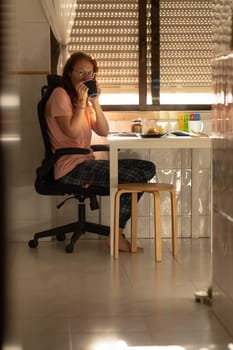 An adult woman drinking coffee at kitchen table - looking in the camera. Vertical shot