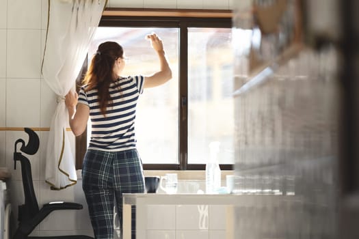 Adult woman housewife washing a window in the kitchen. Mid shot