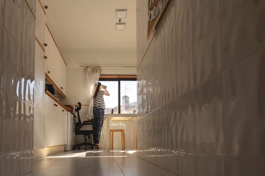 A woman housewife washing windows at the kitchen - lower view from corridor. Mid shot