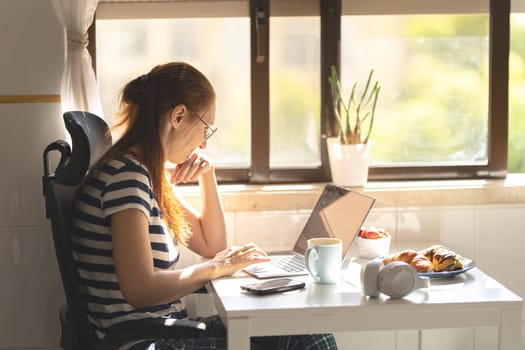 Adult woman freelancer working at the kitchen table. Mid shot