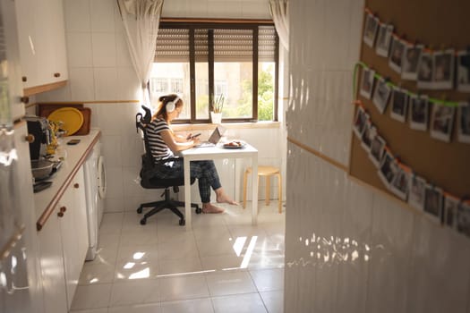 An adult business woman in headphones working at the kitchen. Mid shot