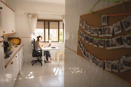 An adult business woman in headphones working at the kitchen - a board with printed photos in the foreground. Mid shot