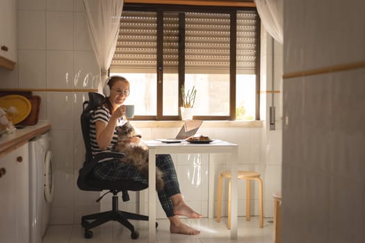 A business woman sitting at the kitchen table with her cat on her laps. Mid shot