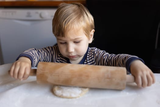 Family cooking - a little boy rolls out dough with a rolling pin. Mid shot