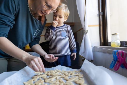 Family making cookies - a woman with her little son sprinkle sugar on the dough. Mid shot