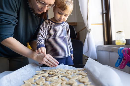 Family making cookies - a woman with her little son sprinkle poppy seed on the dough. Mid shot