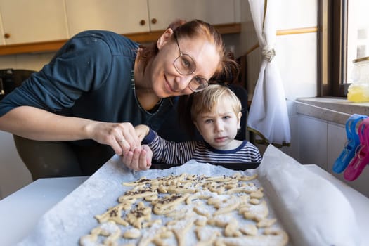 A woman with her little son make cookies in the shape of dinosaurs - looking in the camera. Mid shot