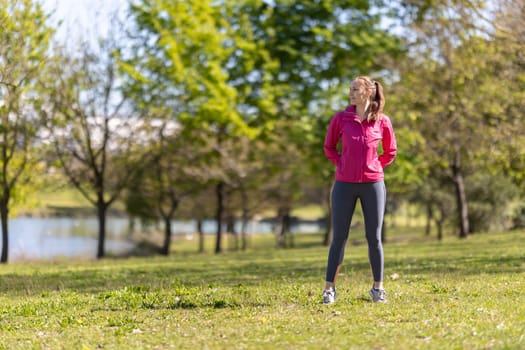 An adult smiling woman in sports clothes standing on the field and looking to the side. Mid shot
