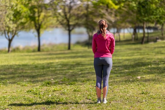 An adult woman in sports clothes standing on the field - view from the back. Mid shot