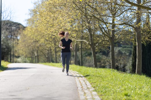 Adult fitness woman jogging on the track in the park. Mid shot