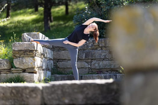 Fitness concept - adult smiling woman does stretching with her leg thrown on the stone wall. Mid shot