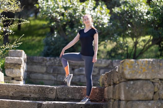 Adult smiling woman in sports clothes in the park. Mid shot