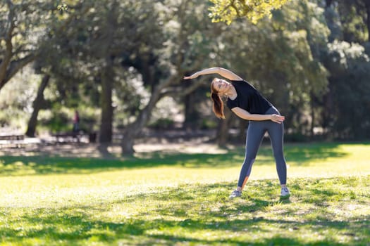 An adult woman in sports doing fitness exercise in the park. Mid shot