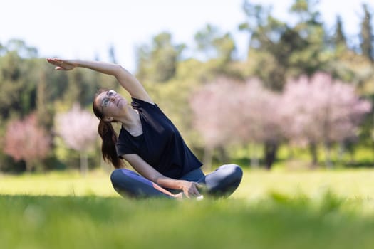 An adult woman sitting in lotus position and bending left. Mid shot
