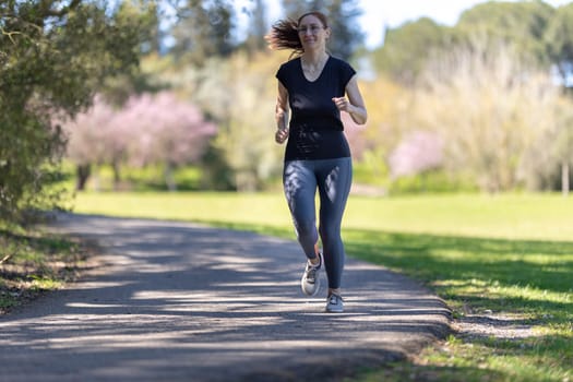 An adult smiling woman in tight grey leggings jogging on nature. Mid shot