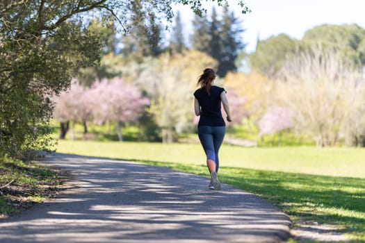 An adult woman in grey leggings jogging on nature. Mid shot
