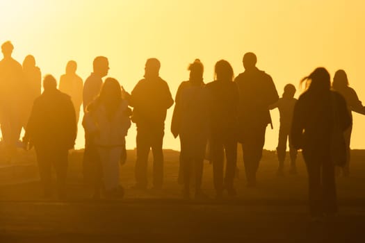 Silhouettes of people in yellow light of a bright orange sunset. Mid shot