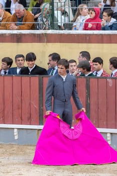 March 26, 2023 Lisbon, Portugal: Tourada - bullfighter wearing grey suit stand on arena holding bright rag. Vertical shot