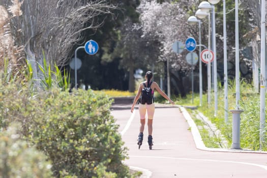 A woman rides roller skates in the park - signs indicating the path for a bicycle and a parent with a child. Mid shot