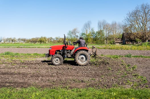 A red tractor on which a farmer sits and cultivates the land for further planting and sowing