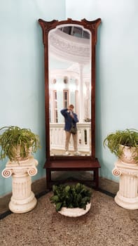 The reflection of a girl or woman in old high mirror and flowers in vases. The hall of the ancient castle with columns