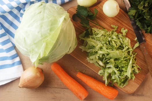 Sliced cabbage on a wooden board with carrots, onions and herbs. Preparing to cook coleslaw