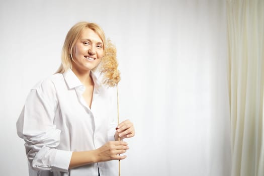 Portrait of a pretty blonde smiling woman with soft ear in hands posing on a white background. Happy girl model in white shirt in studio. The concept of softness, tenderness and dreams. Copy space