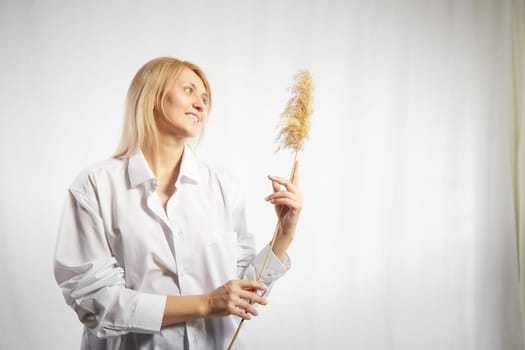 Portrait of a pretty blonde smiling woman with soft ear in hands posing on a white background. Happy girl model in white shirt in studio. The concept of softness, tenderness and dreams. Copy space