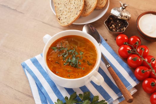 Vegetable soup with potatoes, cabbage, carrots and onions in a white bowl on the kitchen table. Vegetarian food.