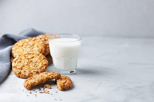 Oatmeal cookies with sesame seeds and flax seeds with a glass of milk on a gray background.Copy space