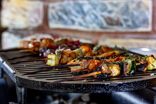 A lot of mini-kebabs of meat, fish, chicken, shrimp, vegetables on wooden skewers are fried on a small cast-iron grill.