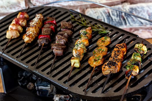 A lot of mini-kebabs of meat, fish, chicken, shrimp, vegetables on wooden skewers are fried on a small cast-iron grill.
