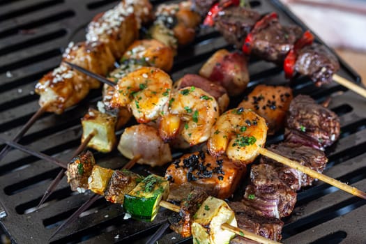 A lot of mini-kebabs of meat, fish, chicken, shrimp, vegetables on wooden skewers are fried on a small cast-iron grill.