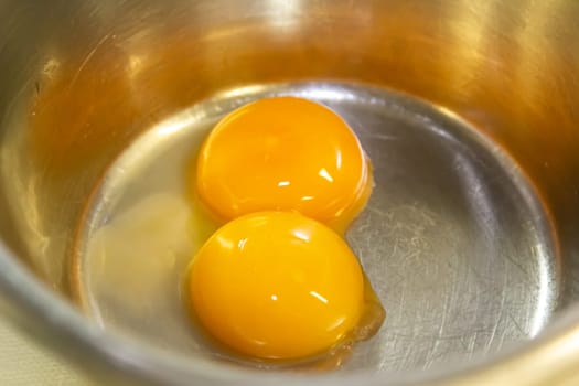 Two egg yolks in a steel bowl for making sauce or omelet.