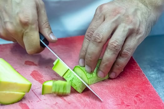 Zucchini being sliced on a red cutting board