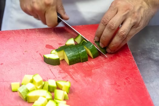 Zucchini being sliced on a red cutting board