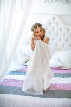 Beautiful girl in white dress standing on bed. High quality photo