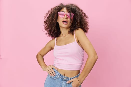 Woman with curly afro hair with sunglasses model poses on a pink background in a pink T-shirt, free movement and dance, look into the camera, smile with teeth and happiness, copy space. High quality photo