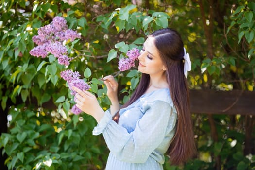 romantic beautiful girl in light blue dress stands nearby blooming lilac bush , in the garden, in sunny day. Close up. copy space