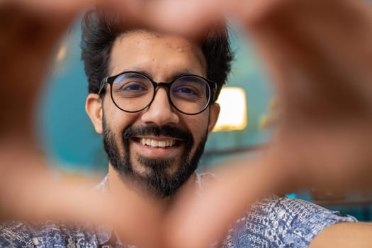 I love you. Happy indian man at home living room couch makes symbol of love, showing heart sign to camera, express romantic feelings express sincere positive feelings. Charity, gratitude, donation