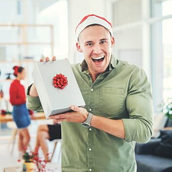 Christmas, coworking office and gift for excited and happy business man during holiday celebration with secret Santa present. Portrait of an employee holding gift box surprise at workplace event.