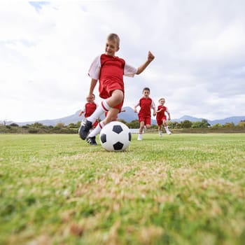 Running, kick and sports with children and soccer ball on field for training, competition and fitness. Game, summer and action with football player on pitch for goals, energy and athlete.