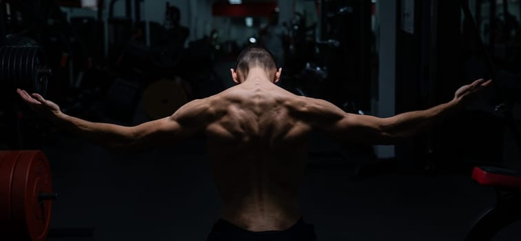 Back view of shirtless man with sculpted body in gym