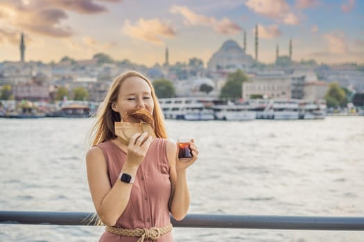 Woman in Istanbul having breakfast with Simit and a glass of Turkish tea. Glass of Turkish tea and bagel Simit against golden horn bay in Istanbul, Turkey. Turkiye.