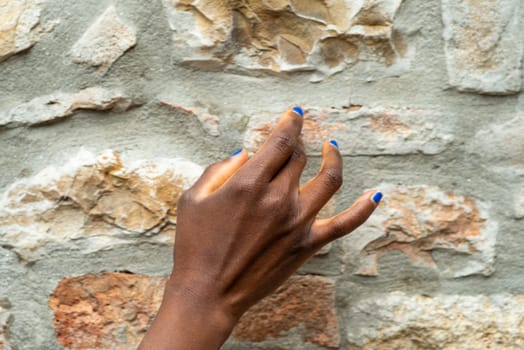 fashionable beautiful hands of african woman with nails paint in blu over a stone old wall