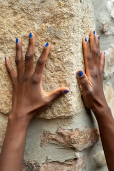 fashionable beautiful hands of african woman with nails paint in blu over a stone old wall