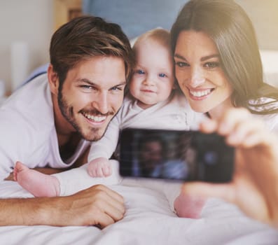 Happy family, parents and selfie of baby on bed in home for love, care and quality time together. Mother, father and newborn child smile for photograph, fun memory and happiness of bonding in bedroom.