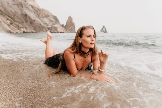 Woman travel sea. Young Happy woman in a long red dress posing on a beach near the sea on background of volcanic rocks, like in Iceland, sharing travel adventure journey