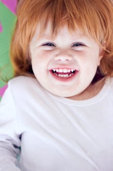 Young girl, laughing and funny portrait of a baby on a home playpen ground with a smile. Ginger infant, kid laugh and happy in a house with joy, youth and positivity from childhood looking up.