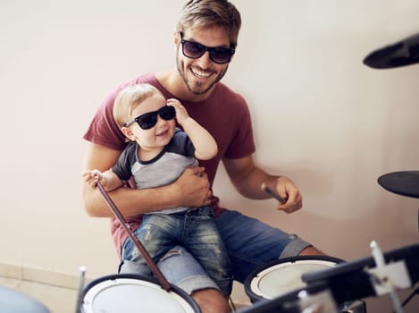 Cool father, baby sunglasses and drummer musician with music development and child learning. Home, happiness and dad with youth drumming lesson with smile, love and parent care at a family house.